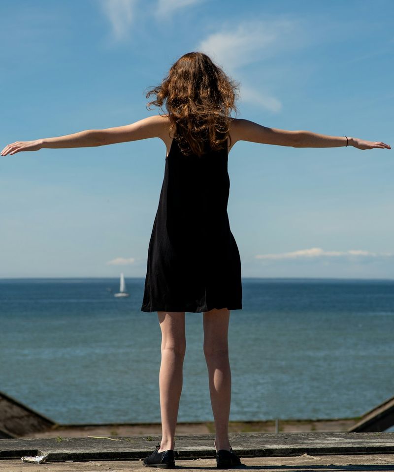 Femme de dos face à la mer, les bras grands ouverts